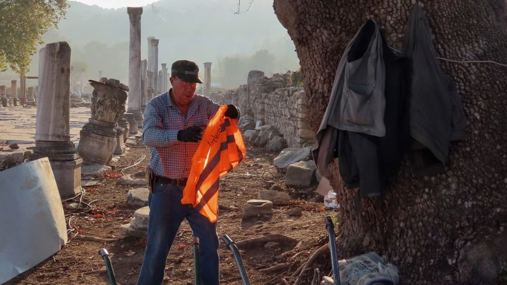 A worker holding an orange vest near ancient ruins in İzmir, showcasing historical architecture.