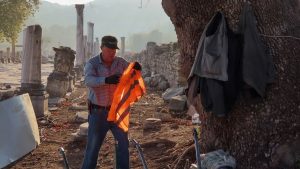 A worker holding an orange vest near ancient ruins in İzmir, showcasing historical architecture.